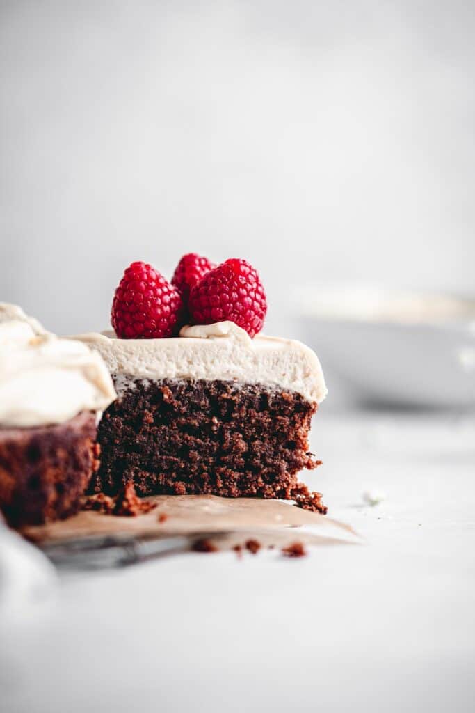 Slice of flourless and gluten free chocolate cake with Irish cream mascarpone frosting, decorated with raspberries.