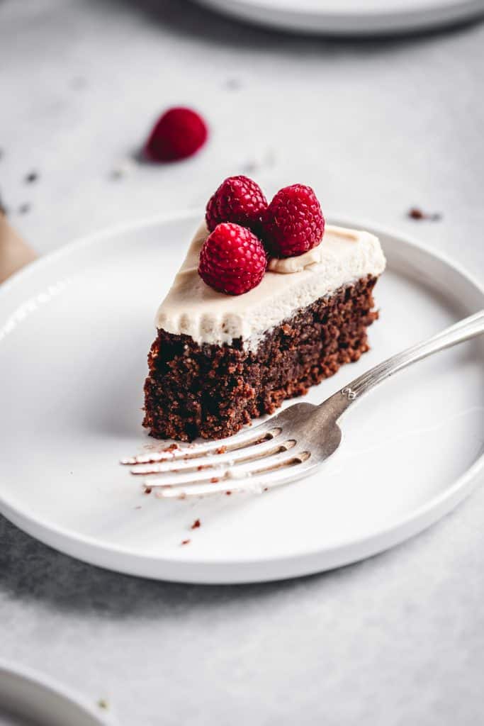 Slice of flourless and gluten free chocolate cake with Irish cream mascarpone frosting, half eaten with a fork.