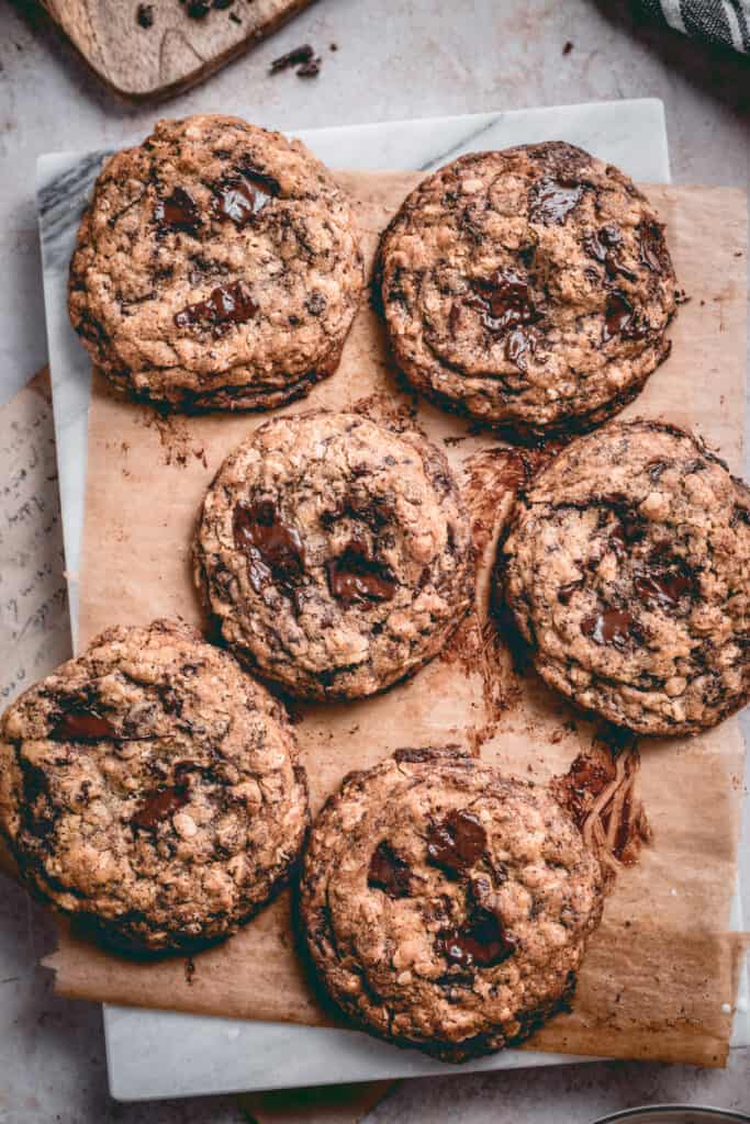 Freshly baked oatmeal chocolate chip cookies on a baking paper, placed on a marble board. 