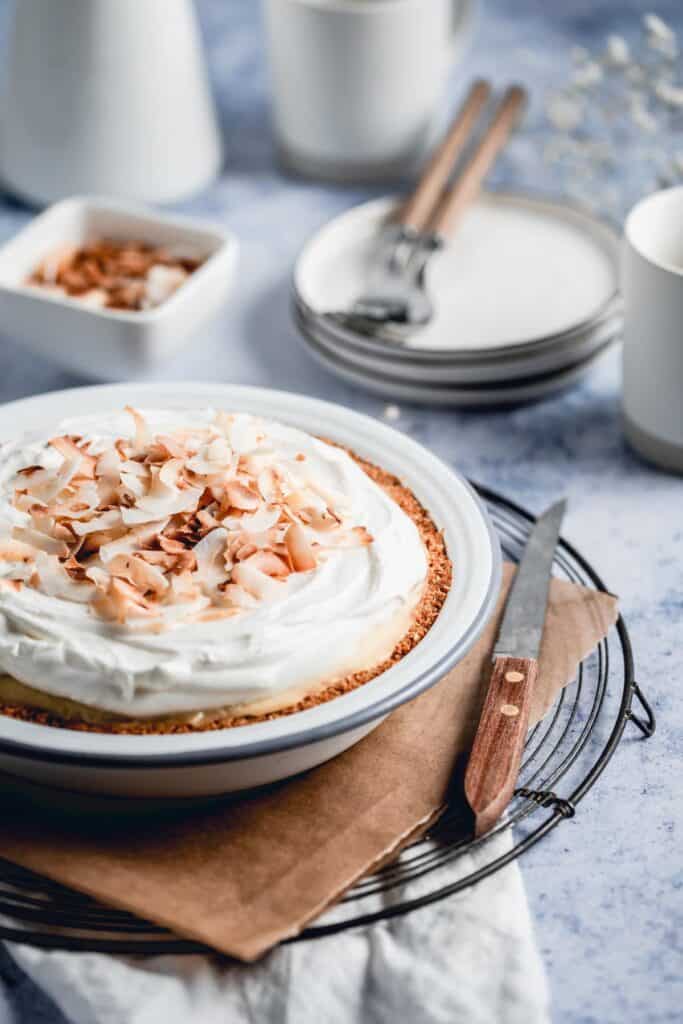 Coconut cream pie served on a wire rack with a knife to cut into it.