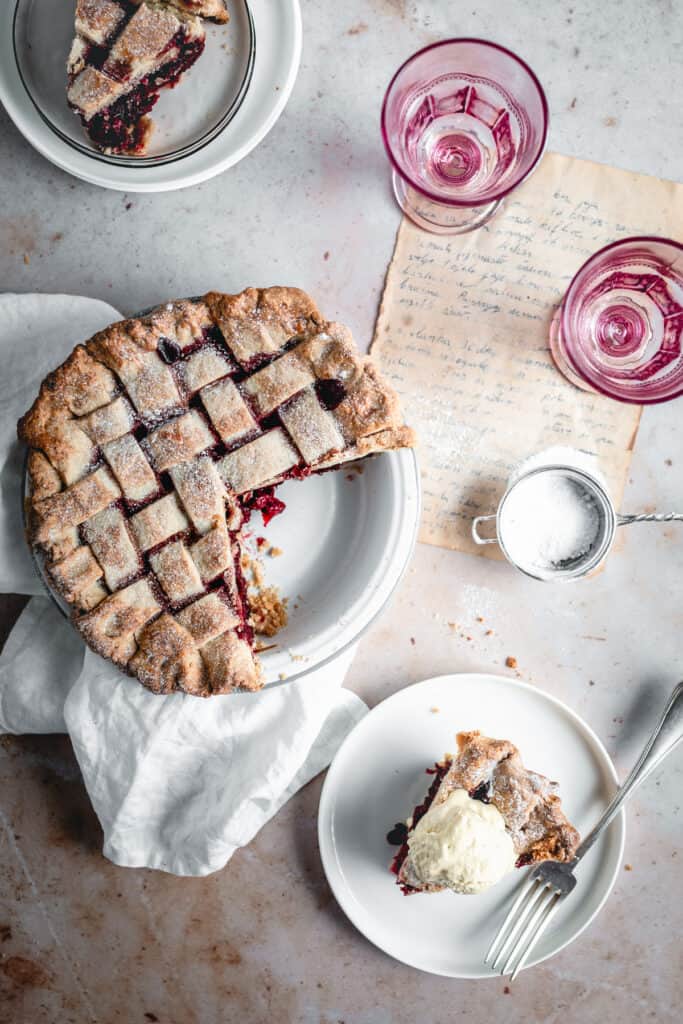 Homemade Cherry Pie with a scoop of ice cream aside, some glasses and plates.