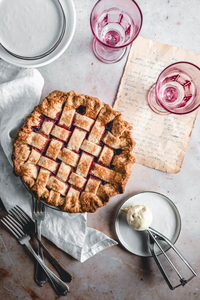 Homemade Cherry Pie with a scoop of ice cream aside, two glasses and plates.