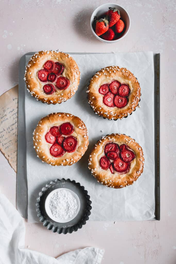 Brioche tarts made with tonka bean pastry cream and strawberries placed on a baking tray.