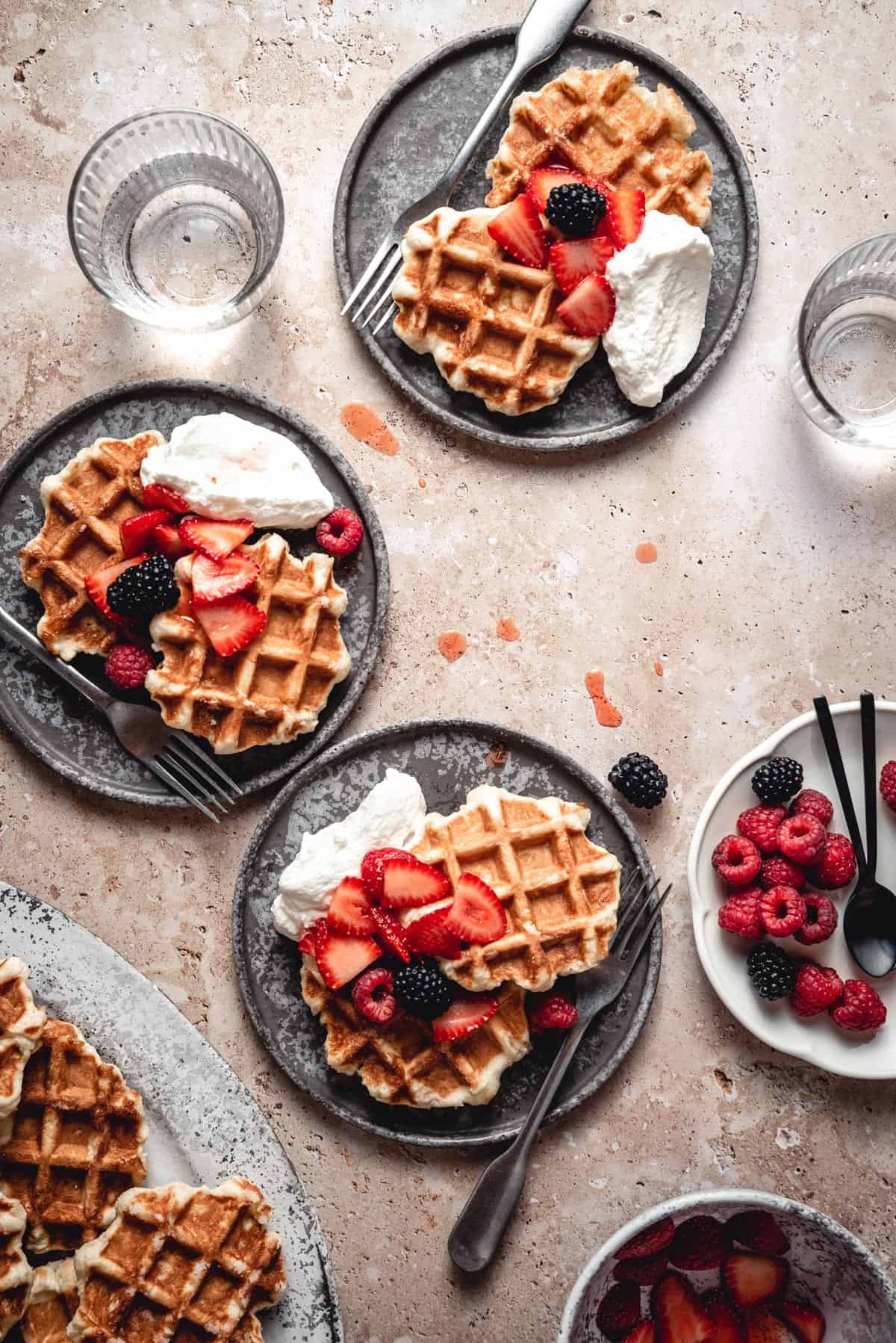 Three plates of waffles served with fresh berries and whipped cream.