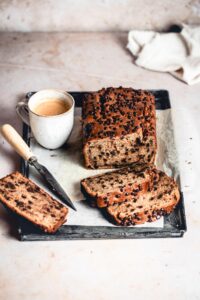 Peanut Butter Chocolate Chip Banana Bread on a tray, with a few cut slices, knife and a cup of coffee.