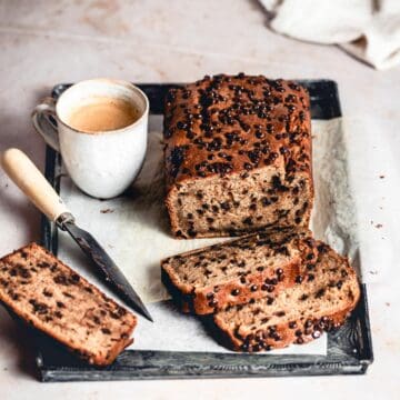 Peanut Butter Chocolate Chip Banana Bread on a tray, with a few cut slices, knife and a cup of coffee.