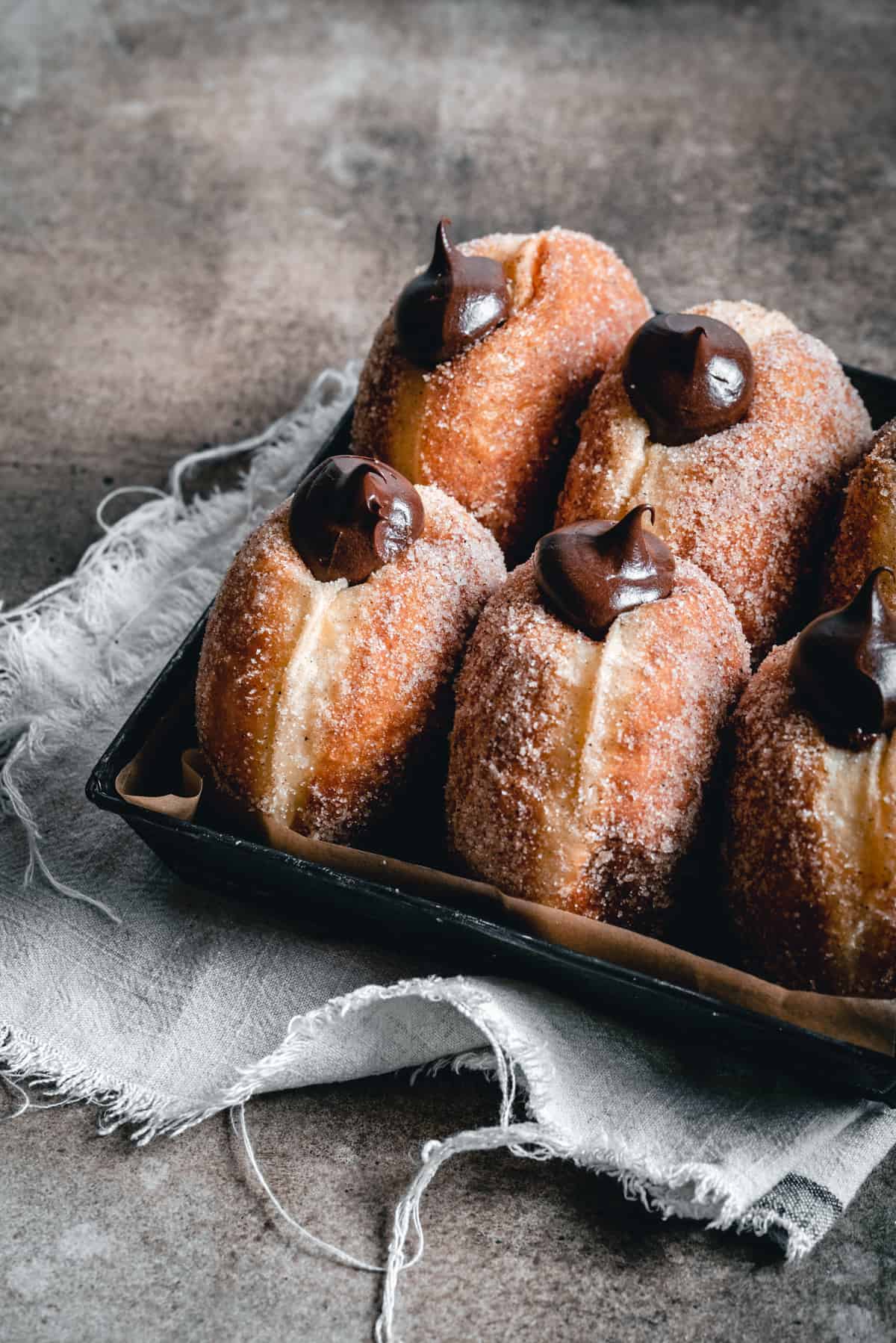 Filled brioche doughnuts placed vertically in a tray with baking paper.