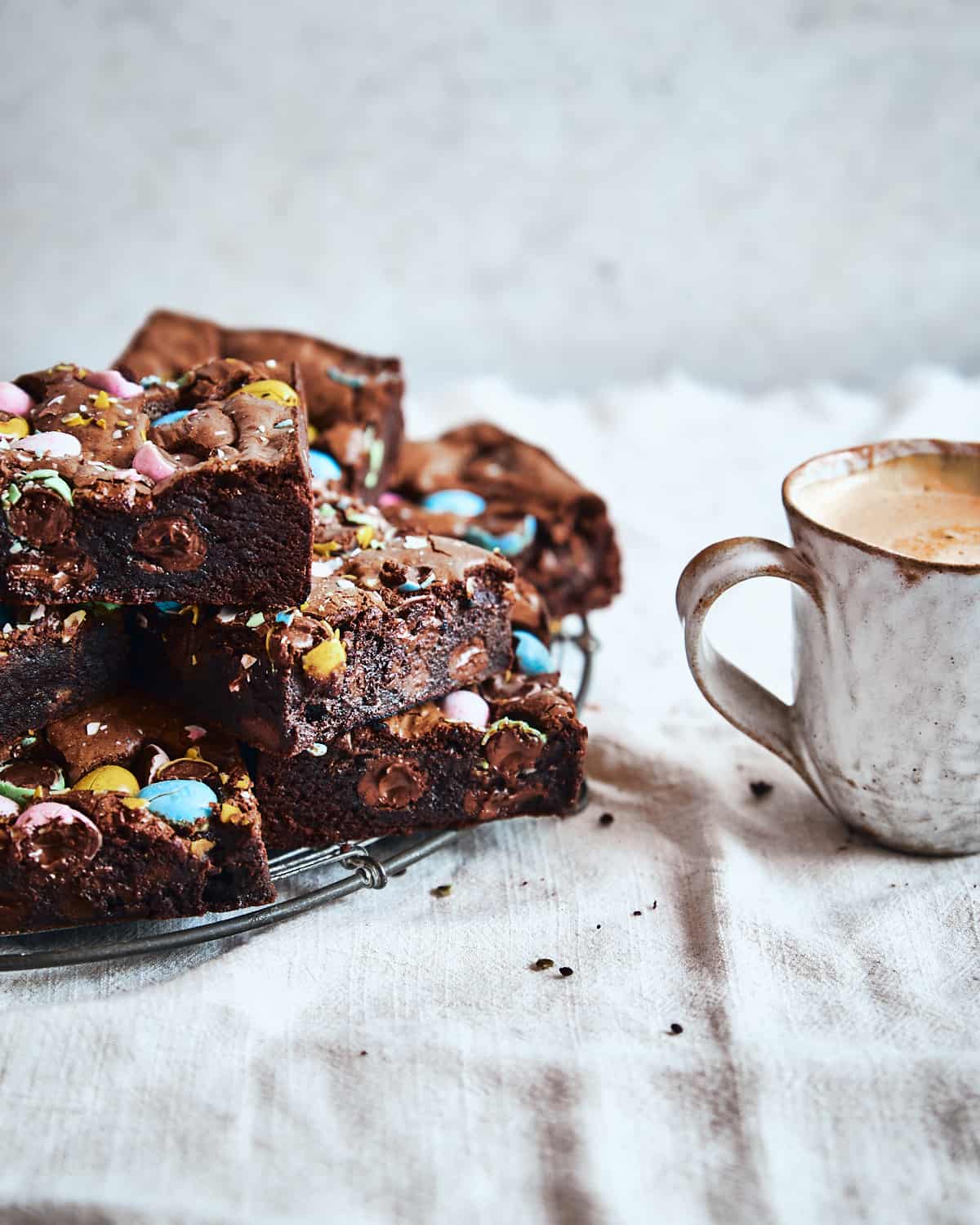 Slices of brownies are served on a cooling rack with a cup of coffee.