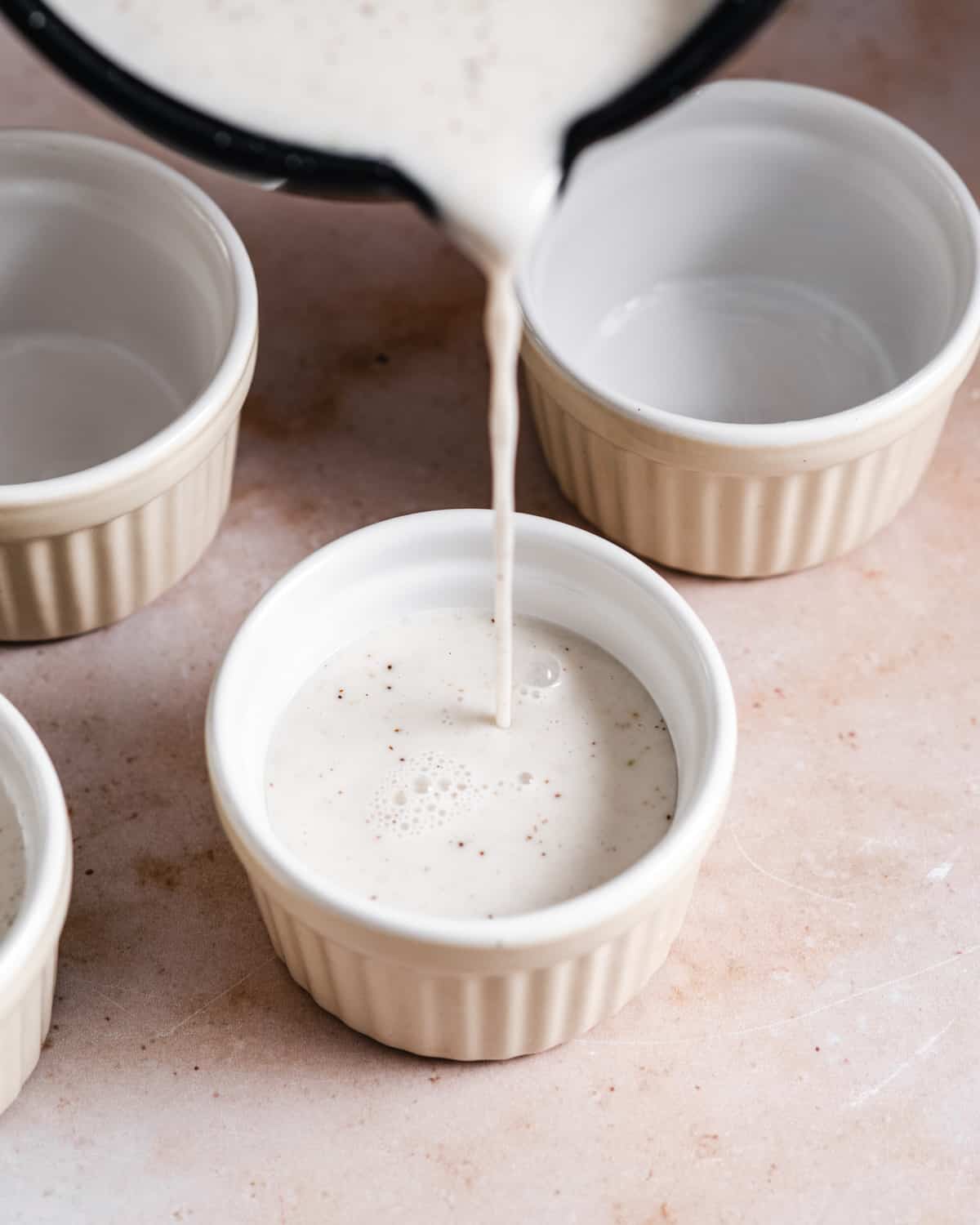 Pouring the coconut milk mixture in the greased ramekins.