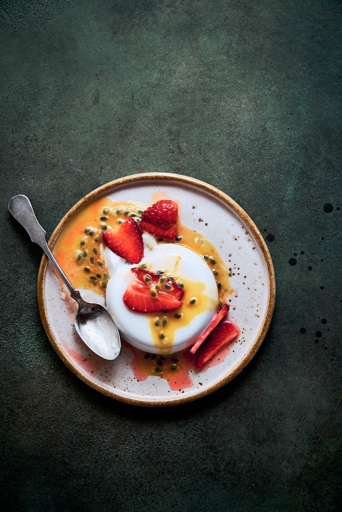 A single serving of coconut panna cotta with passion fruit and strawberries.