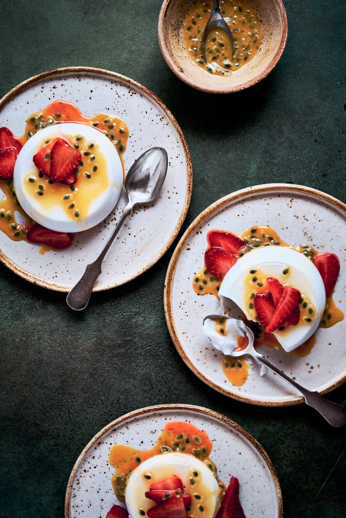 Three plates of coconut panna cotta served with passionfruit and macerated strawberries.